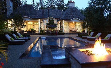 A pool with fire pits and benches in the back yard.