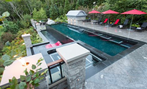 A pool with a large black deck and red umbrellas.