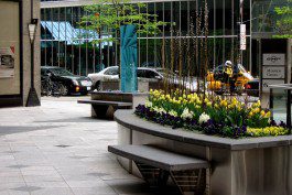 A bench with flowers in it on the side of a sidewalk.