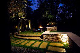 A backyard with a stone walkway and lighting at night.