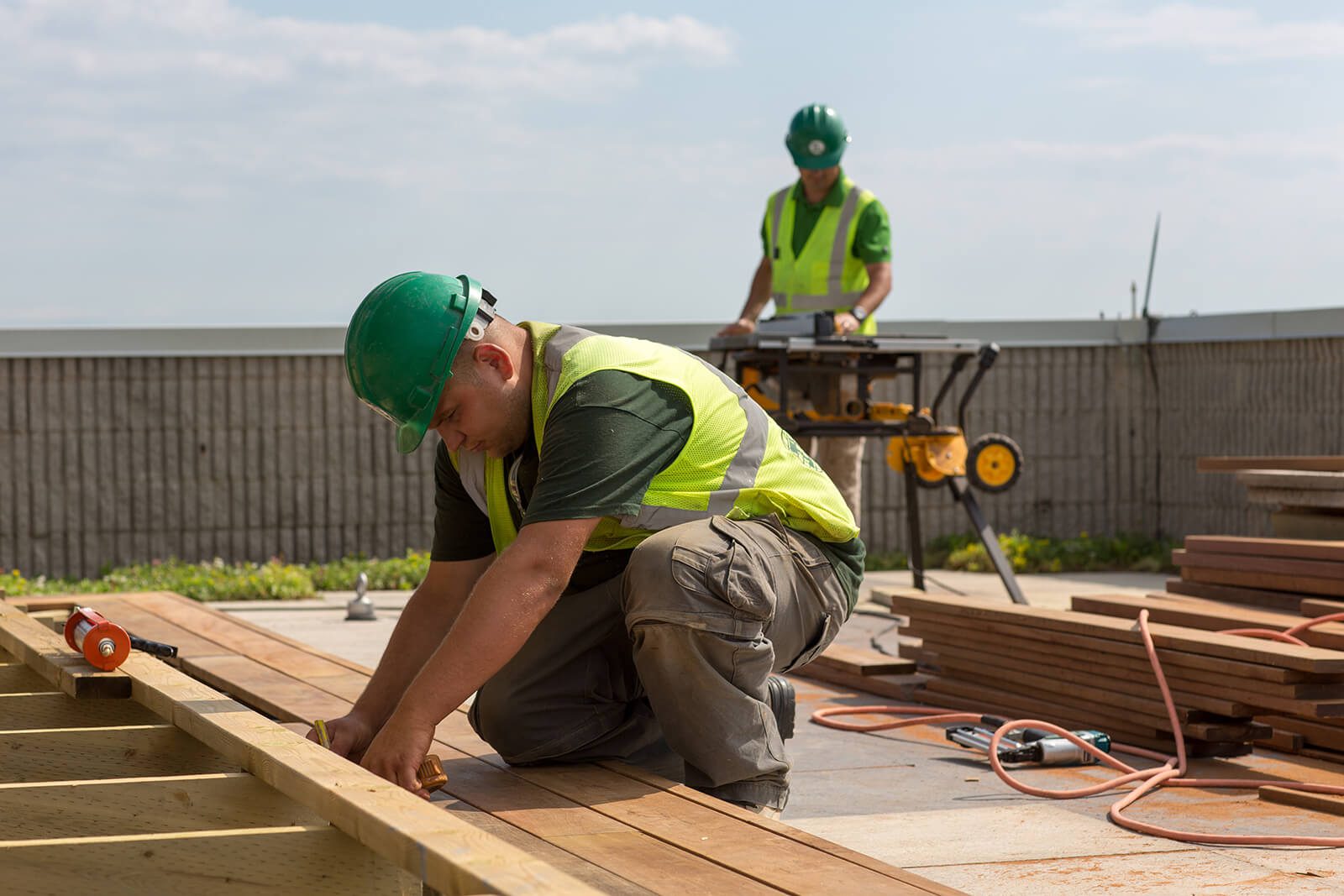 Two men in hard hats and safety vests working on a deck.