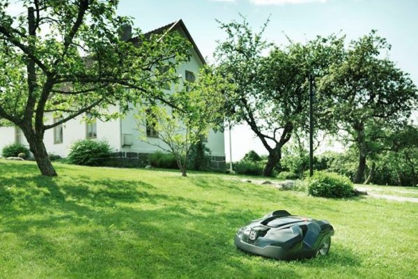 A lawn mower sitting in the grass near a house.