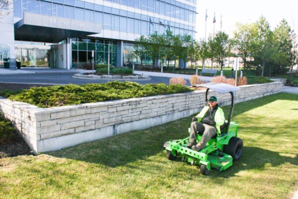 A man riding on the back of a green mower.