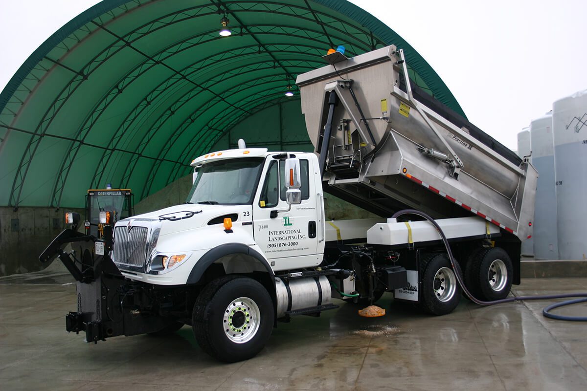 A white dump truck in front of a green building.